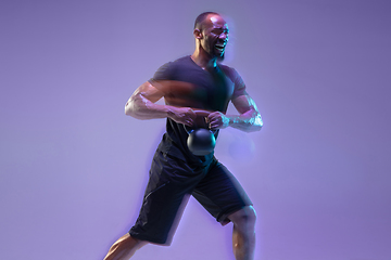 Image showing Young african-american bodybuilder training over purple background in neon, mixed light