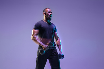 Image showing Young african-american bodybuilder training over purple background in neon, mixed light