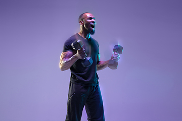 Image showing Young african-american bodybuilder training over purple background in neon, mixed light