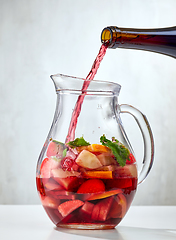 Image showing red wine pouring into jug of cutted fruits