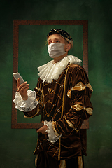 Image showing Young man as a medieval knight on dark background wearing protective mask against coronavirus