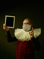 Image showing Senior man as a medieval knight on dark background wearing protective mask against coronavirus