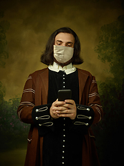 Image showing Young man as a medieval knight on dark background wearing protective mask against coronavirus