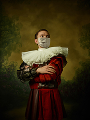 Image showing Young man as a medieval knight on dark background wearing protective mask against coronavirus