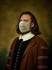 Image showing Young man as a medieval knight on dark background wearing protective mask against coronavirus