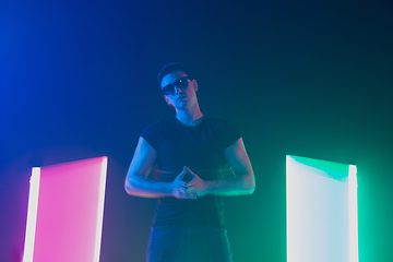 Image showing Young caucasian man posing stylish in neon light on dark background