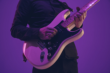 Image showing Young caucasian musician playing guitar in neon light on purple background