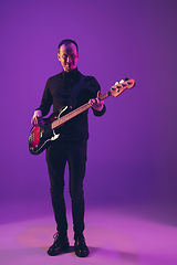 Image showing Young caucasian musician playing guitar in neon light on purple background