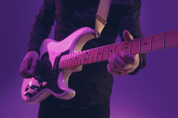 Image showing Young caucasian musician playing guitar in neon light on purple background