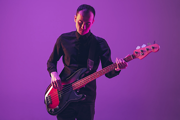 Image showing Young caucasian musician playing guitar in neon light on purple background