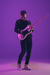 Image showing Young caucasian musician playing guitar in neon light on purple background