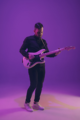 Image showing Young caucasian musician playing guitar in neon light on purple background