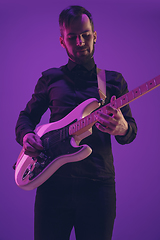 Image showing Young caucasian musician playing guitar in neon light on purple background