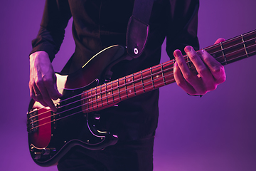 Image showing Young caucasian musician playing guitar in neon light on purple background