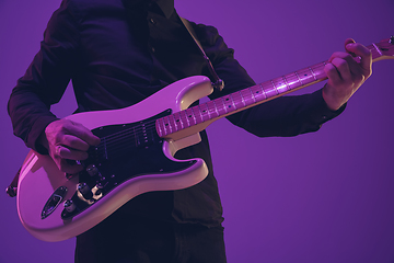 Image showing Young caucasian musician playing guitar in neon light on purple background