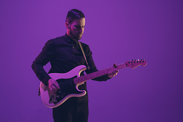 Image showing Young caucasian musician playing guitar in neon light on purple background