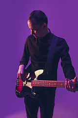 Image showing Young caucasian musician playing guitar in neon light on purple background