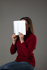 Image showing Happy world book day, read to become someone else - woman covering face with book while reading on grey background