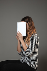 Image showing Happy world book day, read to become someone else - woman covering face with book while reading on grey background