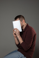 Image showing Happy world book day, read to become someone else - man covering face with book while reading on grey background