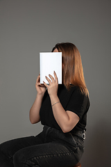 Image showing Happy world book day, read to become someone else - woman covering face with book while reading on grey background