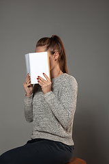 Image showing Happy world book day, read to become someone else - woman covering face with book while reading on grey background