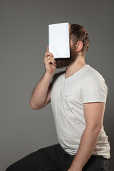 Image showing Happy world book day, read to become someone else - man covering face with book while reading on grey background