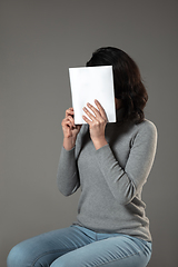 Image showing Happy world book day, read to become someone else - woman covering face with book while reading on grey background