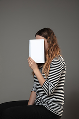 Image showing Happy world book day, read to become someone else - woman covering face with book while reading on grey background
