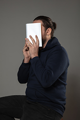 Image showing Happy world book day, read to become someone else - man covering face with book while reading on grey background