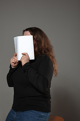 Image showing Happy world book day, read to become someone else - woman covering face with book while reading on grey background