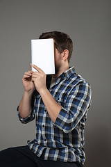 Image showing Happy world book day, read to become someone else - man covering face with book while reading on grey background