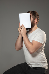 Image showing Happy world book day, read to become someone else - man covering face with book while reading on grey background
