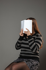 Image showing Happy world book day, read to become someone else - woman covering face with book while reading on grey background