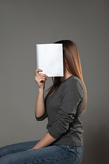 Image showing Happy world book day, read to become someone else - woman covering face with book while reading on grey background