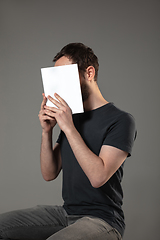 Image showing Happy world book day, read to become someone else - man covering face with book while reading on grey background