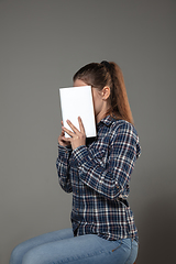 Image showing Happy world book day, read to become someone else - woman covering face with book while reading on grey background