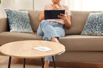 Image showing medical mask on table and woman with tablet pc