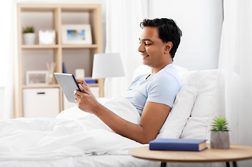 Image showing happy indian man with tablet pc in bed at home