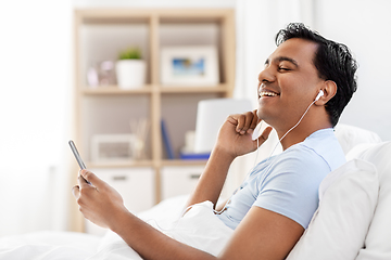 Image showing indian man in earphones with phone in bed at home