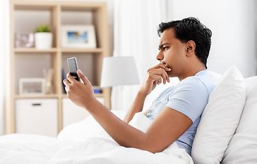 Image showing thinking indian man with smartphone in bed at home