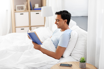 Image showing happy indian man reading book in bed at home