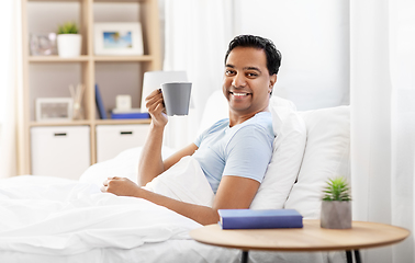 Image showing happy indian man drinking coffee in bed at home