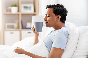 Image showing happy indian man drinking coffee in bed at home