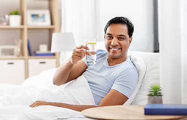 Image showing happy indian man drinking water lying in bed