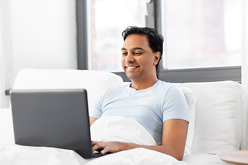 Image showing happy indian man with laptop in bed at home