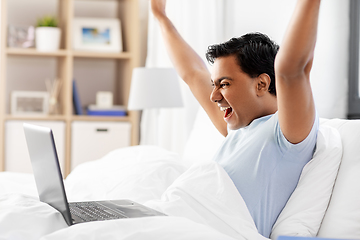 Image showing happy indian man with laptop in bed at home