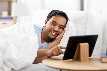 Image showing happy indian man with tablet pc in bed at home