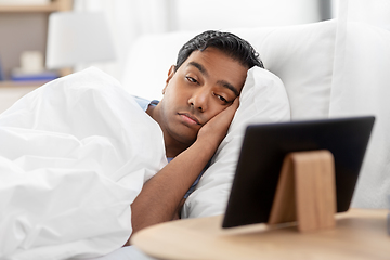 Image showing sleepy indian man looking at tablet pc in bed