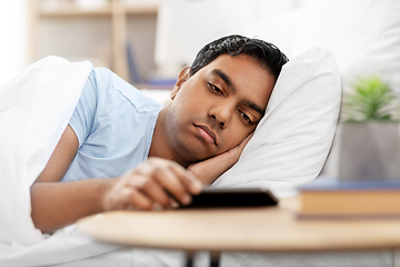 Image showing sleepy indian man in bed looking at smartphone